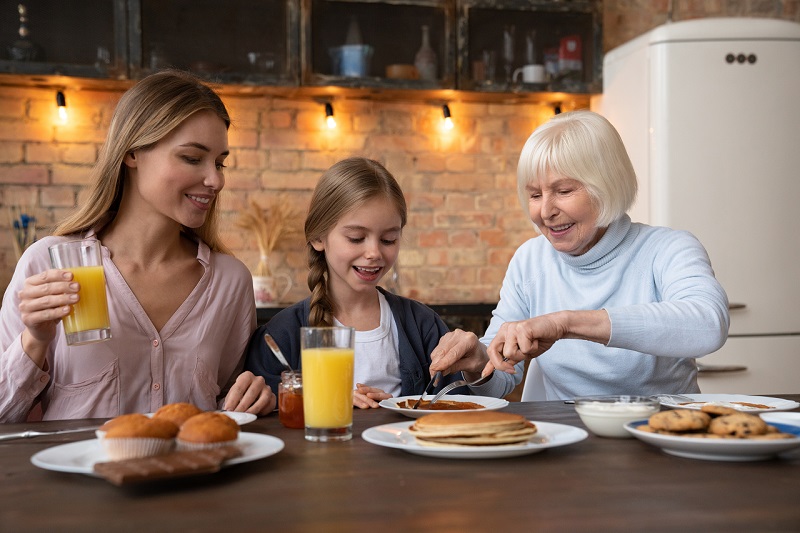 Happy mom, daughter and grandmother eating breakfast in kitchen. Family concept